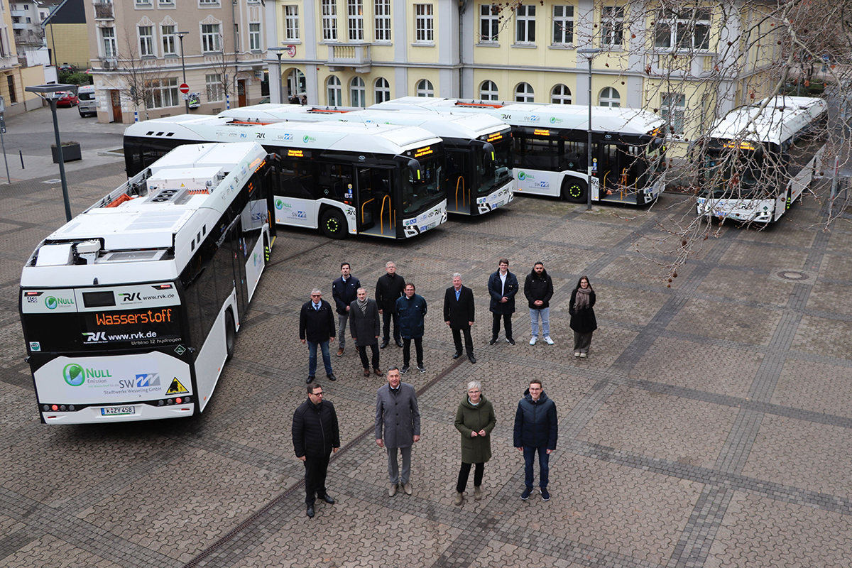 Abbildung der Wasserstoffbusflotte: 5 Busse auf dem Marktplatz und davor beteilite der Stadt Wesseling.